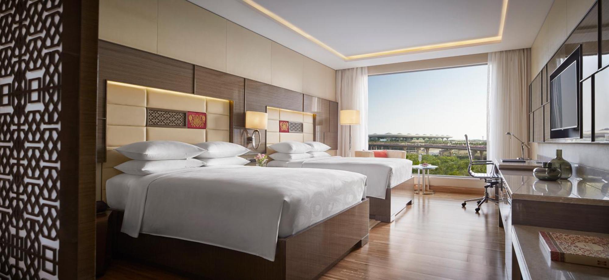 Jw Marriott Mumbai Sahar Airport Hotel Exterior photo The photo shows a well-lit hotel room with two double beds. The beds are neatly made with white linens and several pillows. Each bed has a wooden headboard with decorative panels featuring colorful patterns. 

The room has a large window that offers 